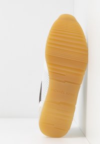 Sneaker bianco con accenti marroni. Presenta una suola testurizzata, pannelli perforati e il marchio "MICHAEL KORS" sul lato. Design a punta rotonda e piatta.
