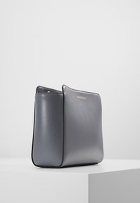 Szara skórzana torebka o teksturowanej powierzchni, z wyraźnie zarysowanym kształtem i minimalistycznym wzornictwem. Dyskretne złote logo z przodu.