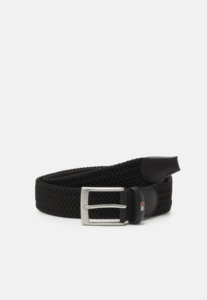 Ceinture en tissu noir tressé avec boucle rectangulaire argentée et extrémités en cuir noir, enroulée sur un fond clair uni.