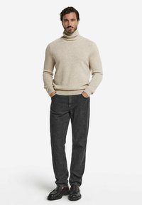 Beige Rollkragenpullover mit geripptem Saum und Bündchen, kombiniert mit dunkelgrauen Hosen und schwarzen Schuhen. Glatte Textur und lässige Passform.