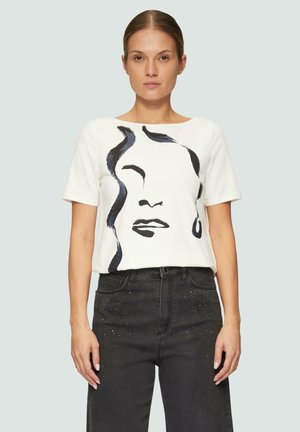 T-shirt blanc à manches courtes présentant un dessin de visage en ligne noire, associé à un jean noir orné de petits clous décoratifs.