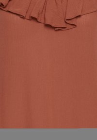 Roestkleurige top van een zachte, lichte stof met een ruffled halslijn detail. Glad textuur met een subtiele glans.