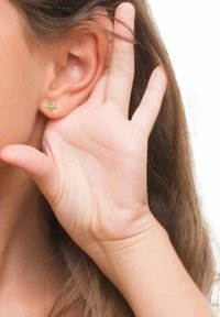 Gul stjärnformad örhänge på ett nära öra, med en hand lyft bredvid. Bakgrunden är enkel och ljusfärgad.