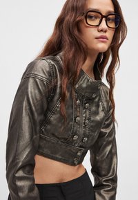 Μεταλλικό cropped μπουφάν με ψηλό γιακά, κουμπιά μπροστά και λεία, υφή, συνδυασμένο με υπερμεγέθη διάφανα γυαλιά.