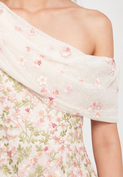 Off-shoulder jurk van doorschijnende witte stof versierd met roze bloemenborduursel bovenop bijpassende stof met groene blaadjespatronen, gedragen door een persoon.