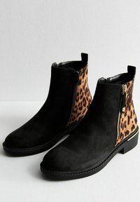 Zwarte suède enkelboots hebben lederen panelen met luipaardprint aan de zijkanten, platte zwarte zolen en gouden ritsaccenten voor eenvoudig aan- en uittrekken.