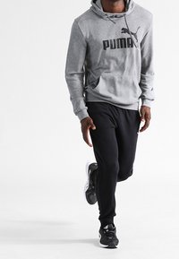 Šedá mikina s kapucí s velkým černým logem Puma, doplněná černými tepláky a černými sportovními botami, s volným střihem.