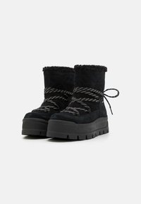 Bottines en suédine noire avec un bord en fausse fourrure, présentant une semelle épaisse et un design lacé croisé avec des lacets contrastants.