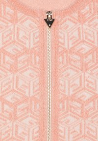 Jasnoróżowy kardigan na zamek błyskawiczny z geometrycznym wzorem w kontrastującym kremowym kolorze. Metalowy zamek błyskawiczny biegnie z przodu z trójkątną zakładką.