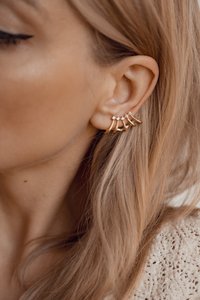 Pendientes de aro dorados que presentan cinco segmentos curvados decorados con pequeñas gemas transparentes, sujetados a la oreja de una persona con el cabello largo y liso.