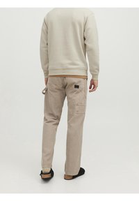 Pantaloni cargo da uomo color beige chiaro con molteplici tasche, vita elastica e vestibilità dritta, abbinati a una felpa di colore neutro.