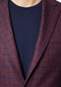 Burgundowa marynarka w kratę z teksturowanej tkaniny, z granatową koszulką z okrągłym dekoltem pod spodem, prezentująca warstwowy, strukturalny design.