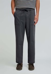 Pantaloni largi, de culoare gri închis, cu talie elastică și șnur. Dispun de două buzunare frontale aplicate și o textură netedă din bumbac.