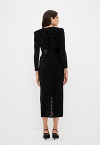 Schwarzes Samtkleid mit floralem Muster, langen Ärmeln, einem Satin-Gürtel und einer mittellangen Länge bis zur Wade. Mit einem Schlitz hinten in der Mitte.