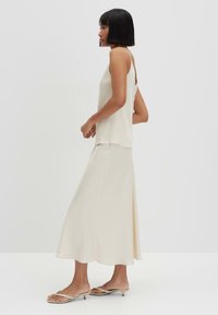 Beige satin camisole paired with a matching midi skirt, featuring thin straps and a flowing silhouette, complemented by simple slip-on sandals.