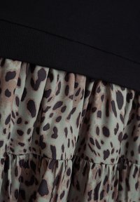 Schwarzes Oberteil mit einem gerippten Bund, das in einen plissierten Rock übergeht, der aus einem grünen Stoff mit einem braunen und schwarzen Leopardenmuster besteht.
