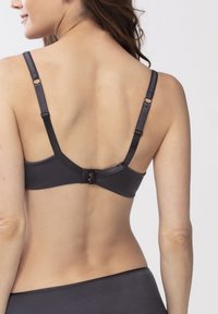 Černá podprsenka s nastavitelnými rameny a zapínáním na háček, vyrobená z hladkého materiálu a s zakřiveným zadním designem. Na materiálu je viditelný jemný lesk.