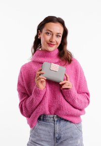 Gray wallet with a pink polka dot accent, held by a person in a fuzzy pink sweater. Features include a soft texture and rectangular shape.