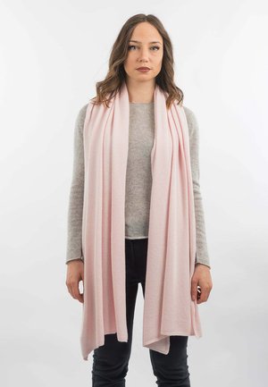 Écharpe enveloppante rose clair en tissu doux, avec une texture lisse et un design drapé, portée sur un pull gris et un pantalon noir.