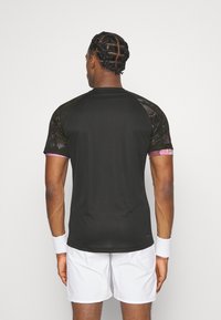 Camiseta atlética negra de manga corta con paneles de malla en los hombros y acentos rosas, combinada con pantalones cortos blancos y muñequeras.