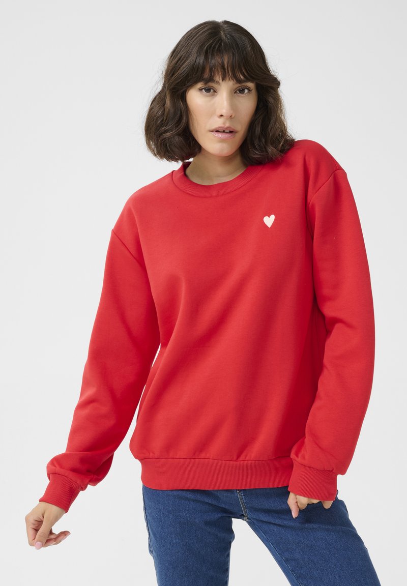 Red sweatshirt in a soft fabric, featuring a round neckline and ribbed cuffs, with a small white heart emblem on the chest.