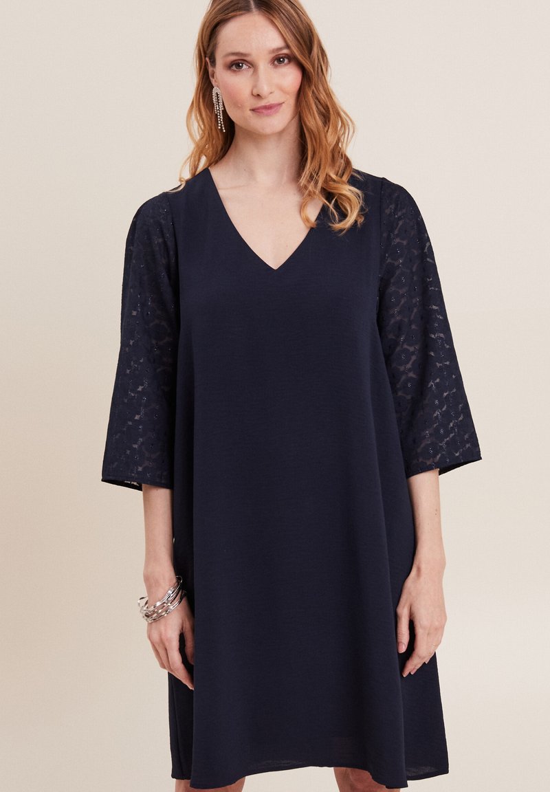 Marineblaues Kleid mit V-Ausschnitt, ¾-langen Spitzenärmeln und lockerer Passform. Glatte Textur mit einem subtilen Glanz im Spitzenmuster.