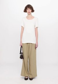White short-sleeve t-shirt paired with beige wide-leg trousers. Model holds a small dark handbag. Simple, casual silhouette.