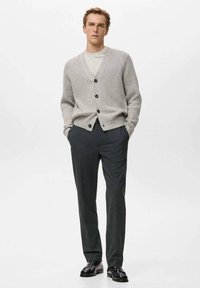 Szary prążkowany kardigan z dekoltem w serek, z sześcioma czarnymi guzikami, zestawiony z dopasowanymi ciemnymi spodniami i czarnymi butami, na jednolitym tle.