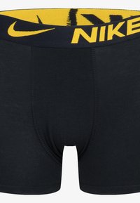 Black cotton boxer briefs with a thick navy and yellow waistband featuring the Nike logo. Smooth texture, mid-length design.