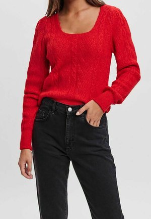 Roter Strickpullover mit quadratischem Ausschnitt, strukturiertem Muster und langen Ärmeln, kombiniert mit hochgeschnittenen schwarzen Jeans.