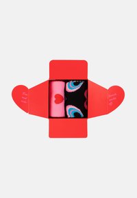 Červená krabička s dvoma pármi ponožiek: jedny ružové s červeným srdcom, druhé čierne s farebnými očkovými vzormi. Krabička má klapky v tvare srdca.