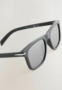Szare plastikowe okulary przeciwsłoneczne z ciemnymi soczewkami, kanciasta konstrukcja oprawki, cienkie metalowe akcenty na zawiasach oraz matowe wykończenie na ramionach.