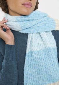 Sciarpa a righe di un blu chiaro e crema, realizzata in morbido materiale testurizzato, avvolta attorno a un maglione scuro, caratterizzata da una combinazione di strisce orizzontali.