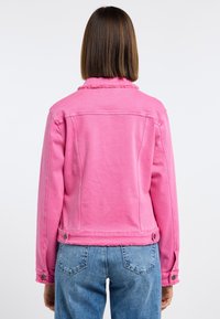 Chaqueta de mezclilla rosa con un dobladillo deshilachado y cuello, con detalles de botones y un diseño ajustado. Llevada con pantalones vaqueros de color azul claro.