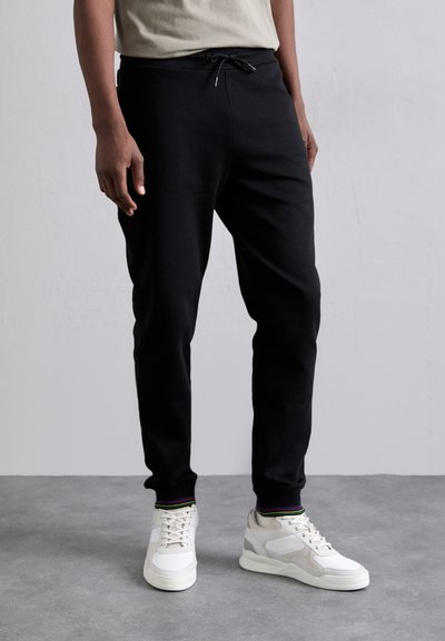 Pantalons de jogging noirs en tissu doux, dotés d'une taille ajustable avec cordon de serrage. Associés à des baskets blanches avec des accents colorés.