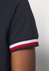 Navy polo met een gestructureerde stof, korte mouwen met rode, witte en zwarte streepmotieven op de manchetten.