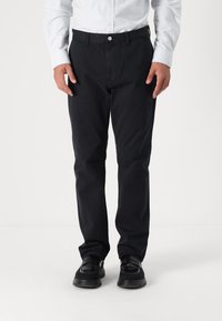Black trousers made of cotton blend, featuring a straight-leg design and front pockets. Paired with polished black loafers.