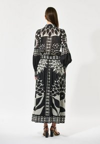 Long black and cream patterned dress with long sleeves, a fitted waist, and floral designs. Textured fabric with a flowing skirt.
