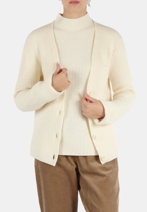 Cardigan a coste crema con maniche lunghe, chiusura frontale con bottoni e un design testurizzato, indossato sopra un maglione a collo alto coordinato.