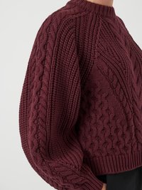 Burgundi színű, kötött pulóver kerek nyakkal, texturált bordázással és puffosujjakkal, puha, vastag fonalból készült.
