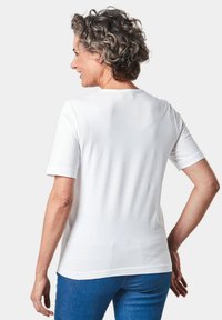 Witte T-shirt met korte mouwen van zacht katoen met een ronde halslijn en een gladde textuur, gedragen met blauwe spijkerbroeken. Heeft een eenvoudig ontwerp.
