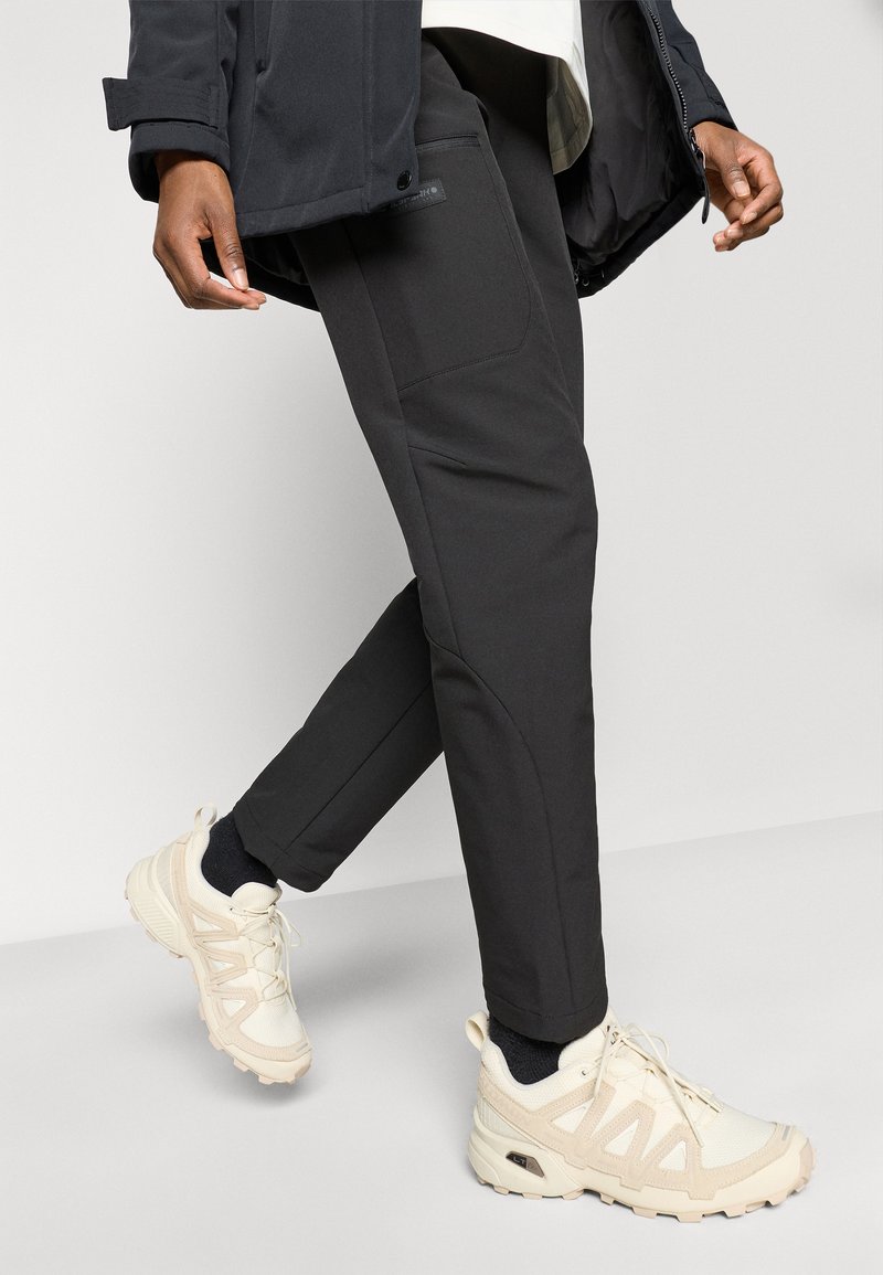 Pantalons de yoga noirs avec poches latérales, associés à des baskets beige clair avec des semelles texturées et des accents en maille.