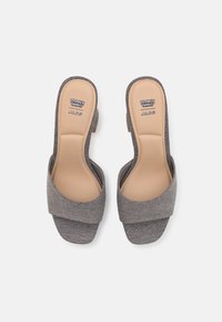 Sandales à enfiler en tissu gris avec une large bande croisée, talon ouvert et semelle intérieure beige légèrement rembourrée. Présentent un logo Looney Tunes et ALDO.