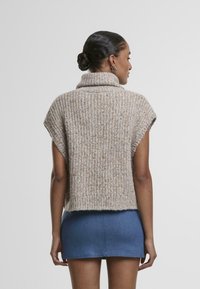 Pull en tricot beige avec un col haut à côtes et des manches courtes, présentant un motif texturé et un ourlet brut, associé à une mini-jupe en denim.