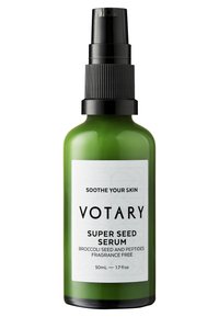 Grön glasflaska med Votary Super Seed Serum och en svart spraymunstycke. Etiketten har en vit bakgrund med svart text och geometriska mönster.