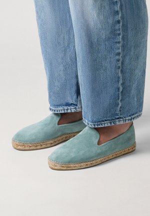Hellblaue Wildleder-Espadrilles zum Hineinschlüpfen, getragen mit hellblauen Jeans, mit natürlicher Jutesohle und minimalistischem Design.
