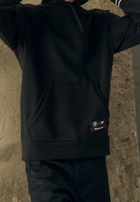 Felpa nera con cappuccio realizzata in tessuto morbido, dotata di tasca frontale e una toppa BMW Motorsport con accenti rossi e blu.