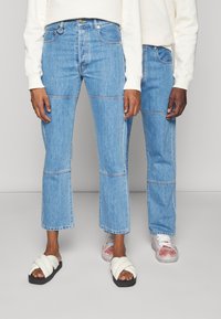 Světle modré džínové kalhoty se rovnými nohavicemi, s viditelnými švy a panelovými detaily, nošené s bílou a černou obuví.