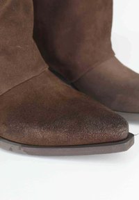 Stivali alla caviglia in suede marrone con punta affusolata, texture liscia e tacco basso e angolare. Presentano una silhouette elegante e un design minimalista.