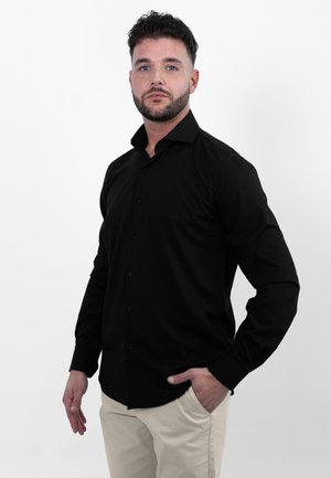 Zwarte lange mouwen knoopsluiting shirt van gladde stof, met een puntige kraag en een getailleerd ontwerp, gecombineerd met lichtbeige broek.